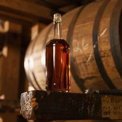 An unlabeled bottle of bourbon sits atop a wooden barrel