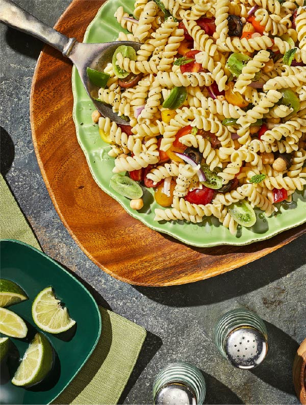 A bowl of delicious and colorful pasta sits atop a wooden table