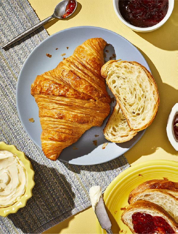 Flaky croissants on a plate surrounded by jams and butter