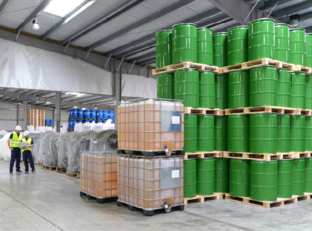 Green 55 gallon barrels stacked in a large warehouse